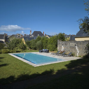 Élégante piscine 11x5m avec liner gris clair, margelles en travertin et volet immergé. Confort et technologie réunis pour un espace raffiné – Bonheur Piscines.